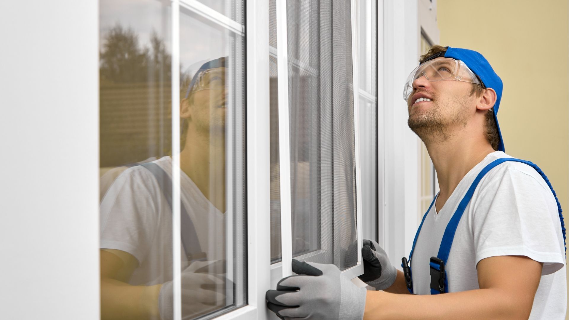 Worker in blue cap and gloves inspecting a window frame outdoors