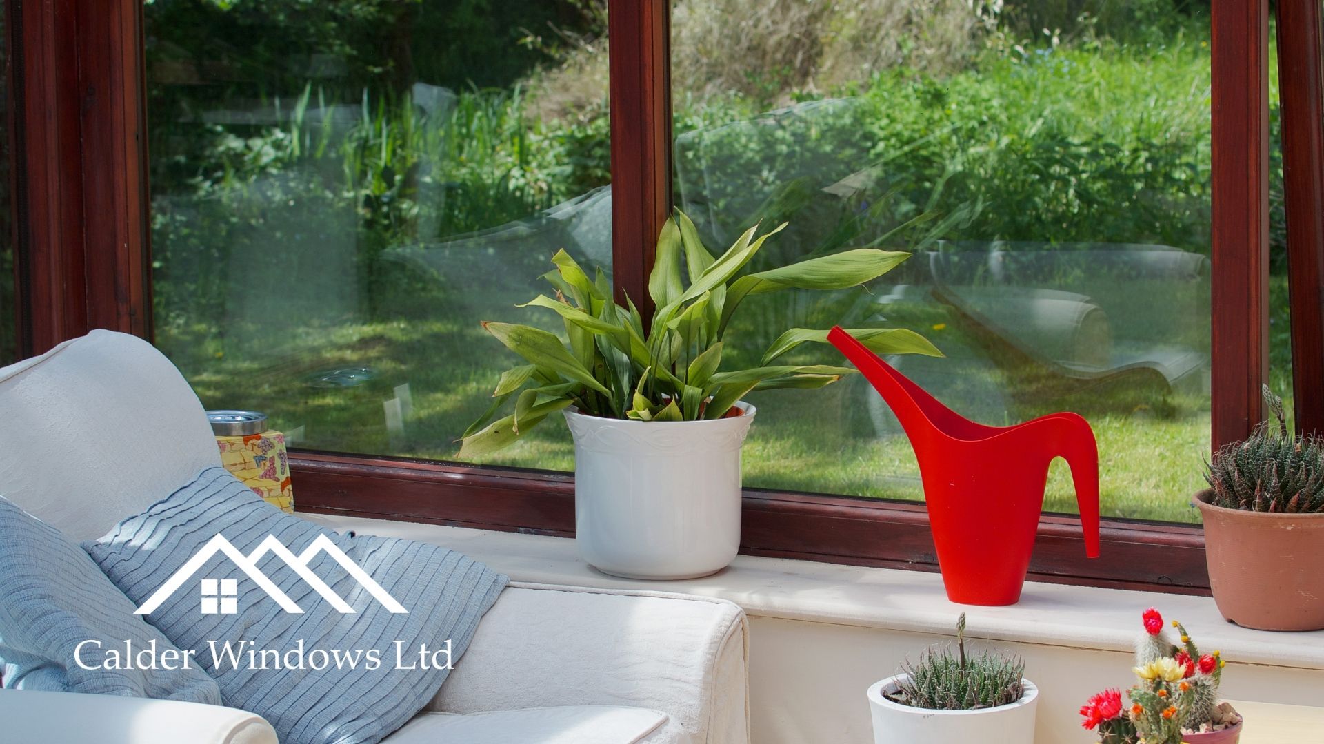 Bright sunroom with potted plants, a red watering can, and green garden views through large windows