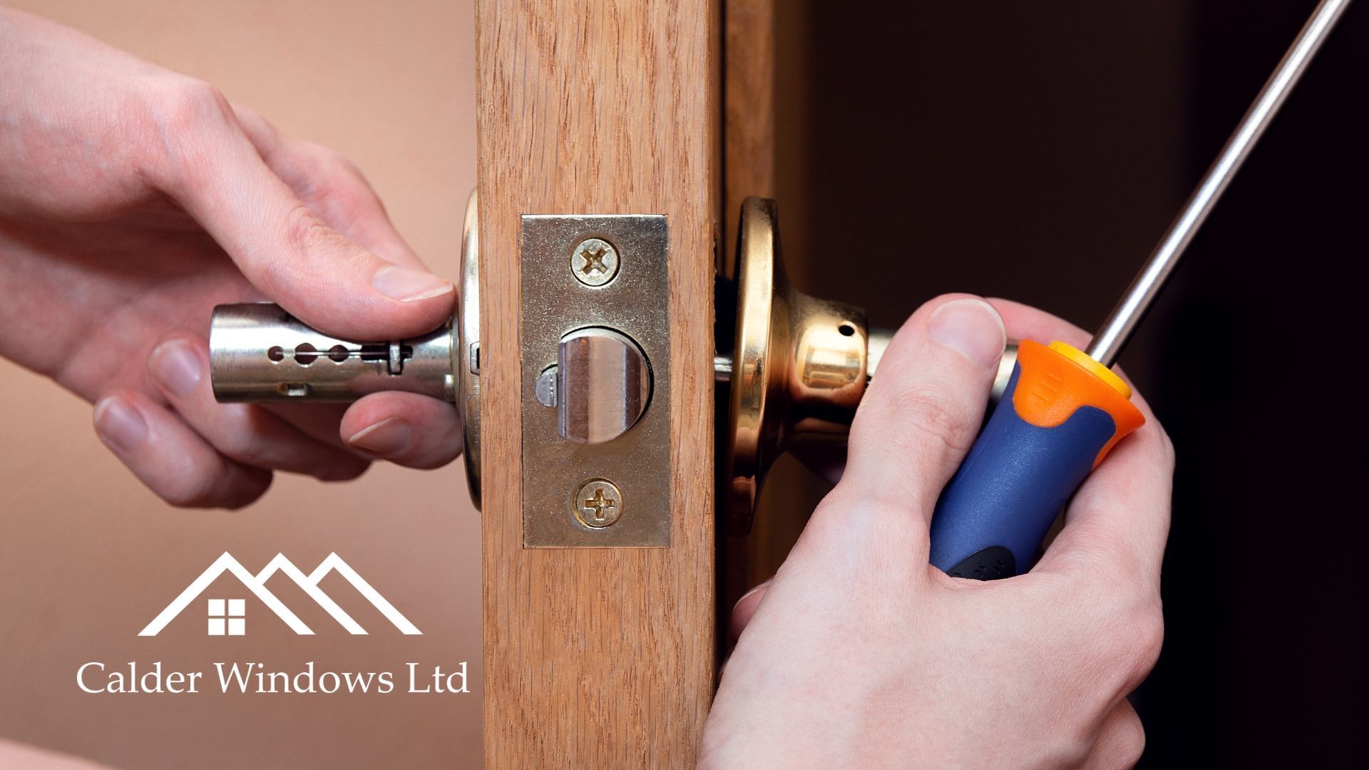 Hands using a screwdriver and lock cylinder to install a brass door lock on a wooden door
