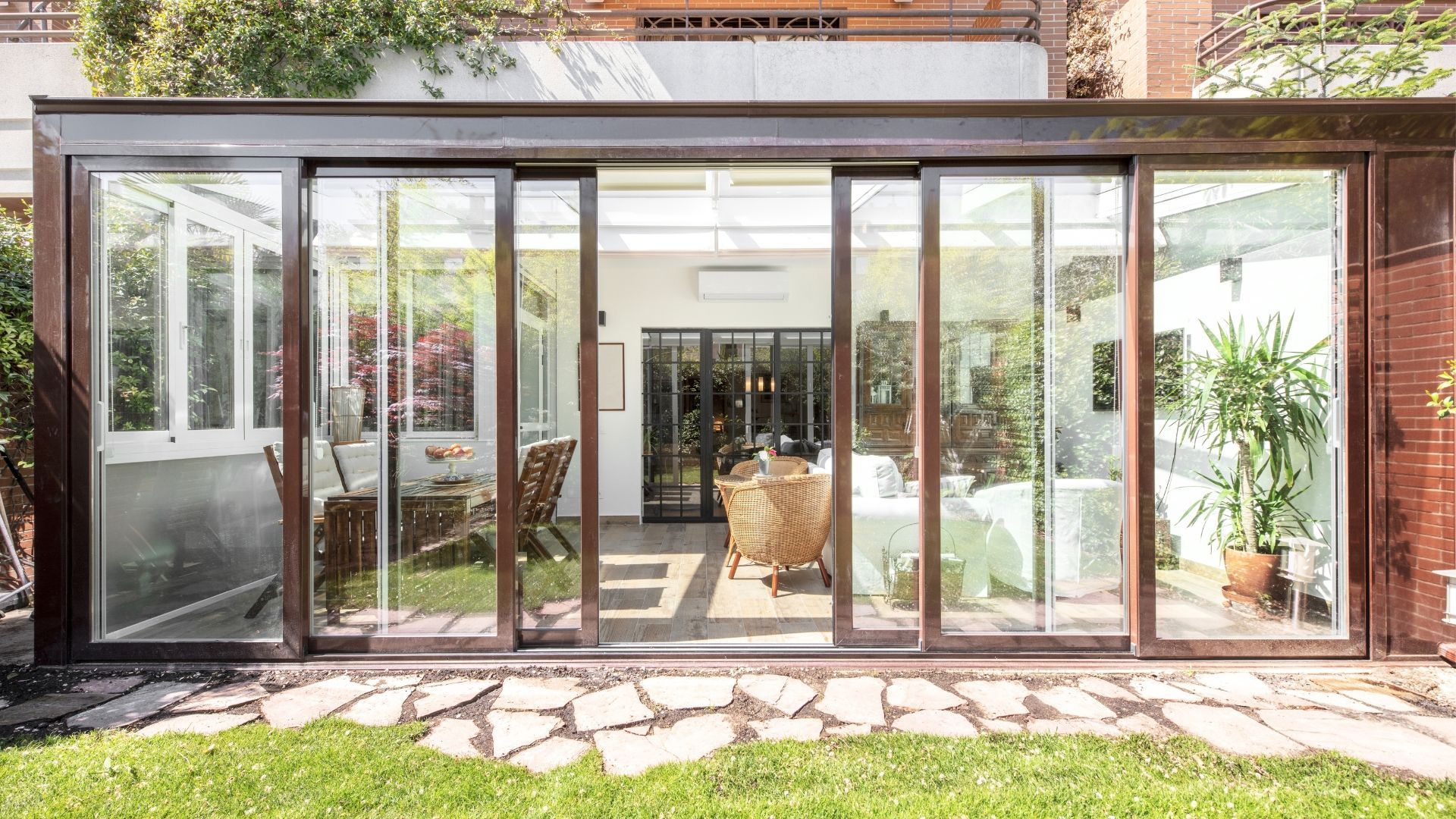 Glass-enclosed patio with sliding doors opening to a bright interior and garden outside