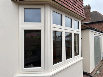 White house bay window with multiple glass panes and a sloped red-tiled roof wall.