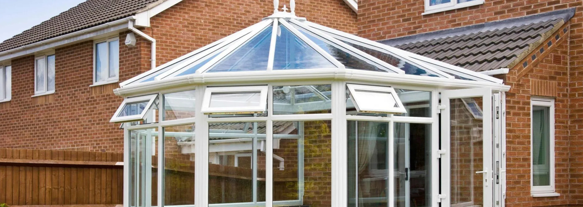 White conservatory attached to a red brick house with a tiled roof and fenced yard