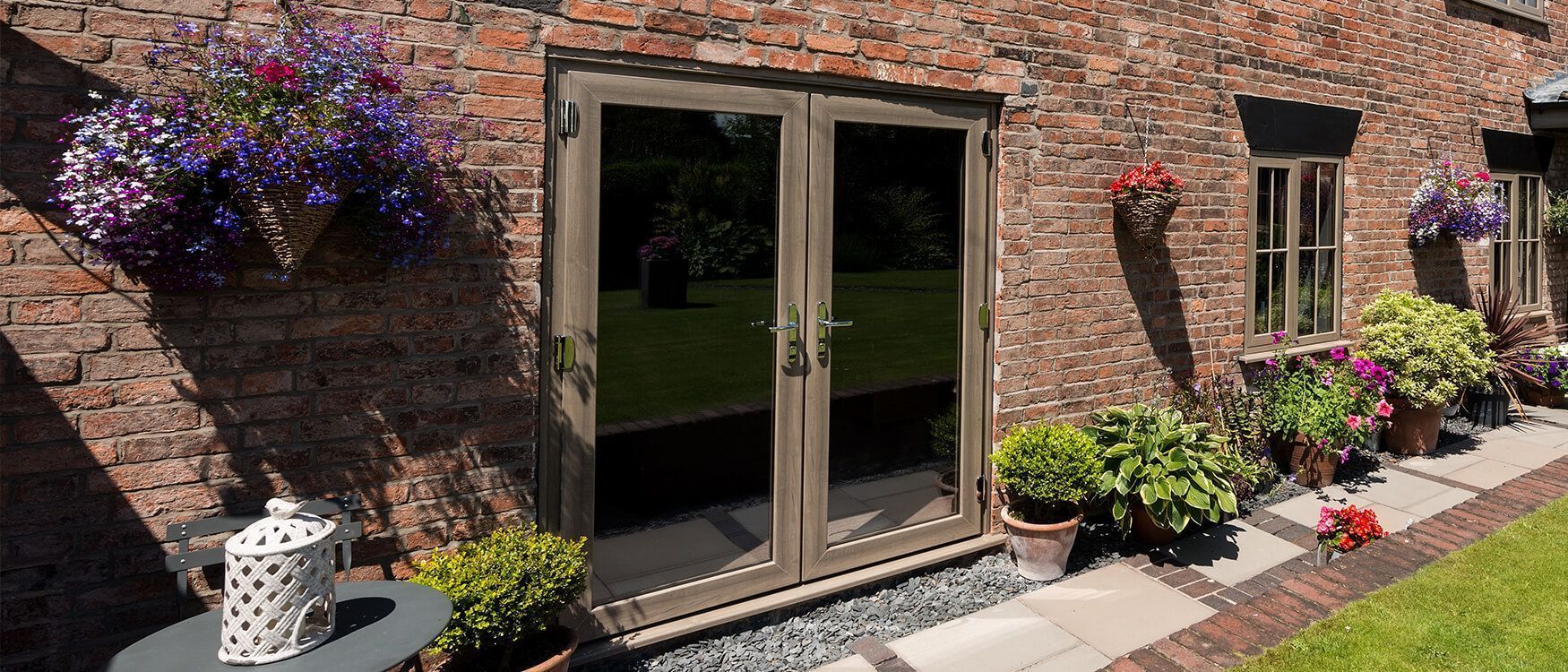 Brick patio with open glass doors, hanging purple flowers, and potted plants along the wall