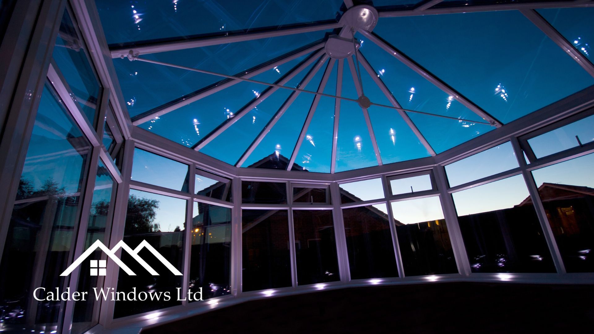 Glass-roofed conservatory at dusk with blue sky and hanging string lights