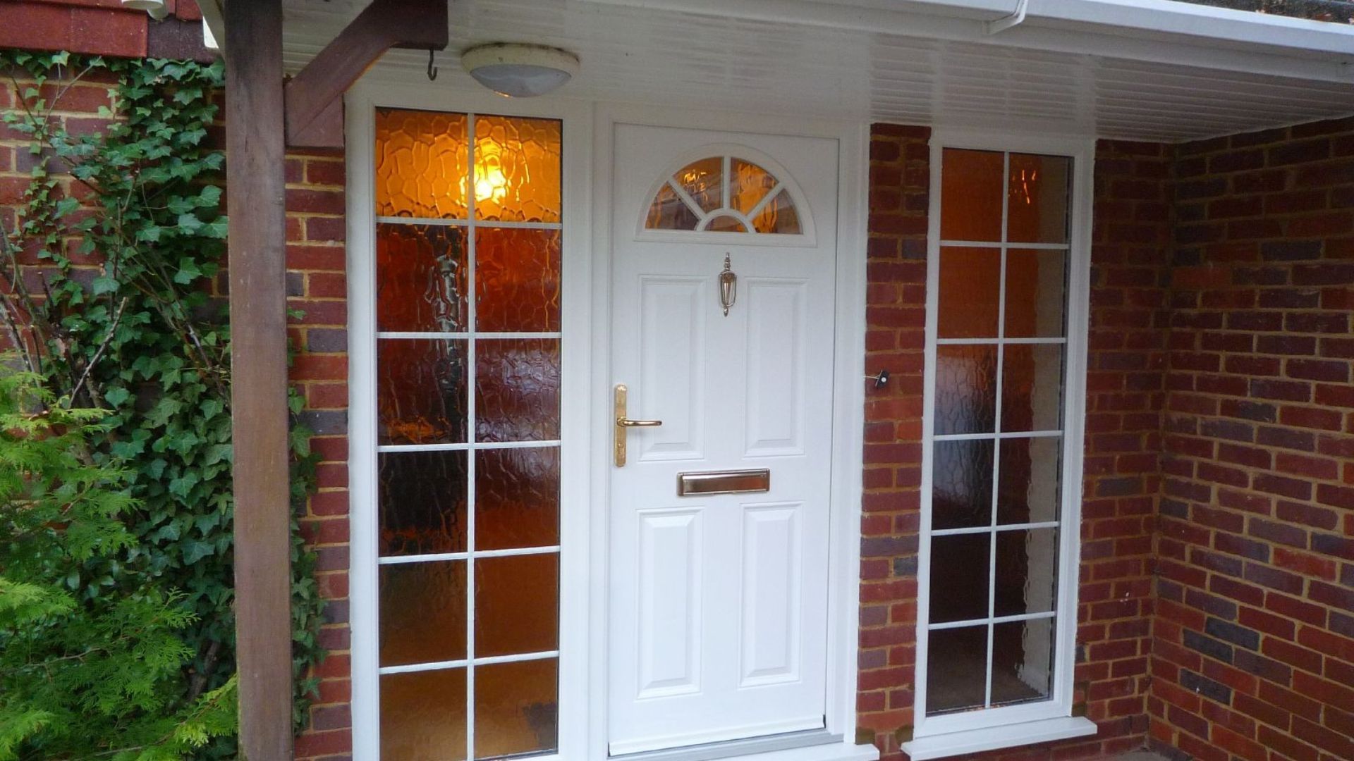 White front door with sidelights and a warm porch light in a red brick entryway