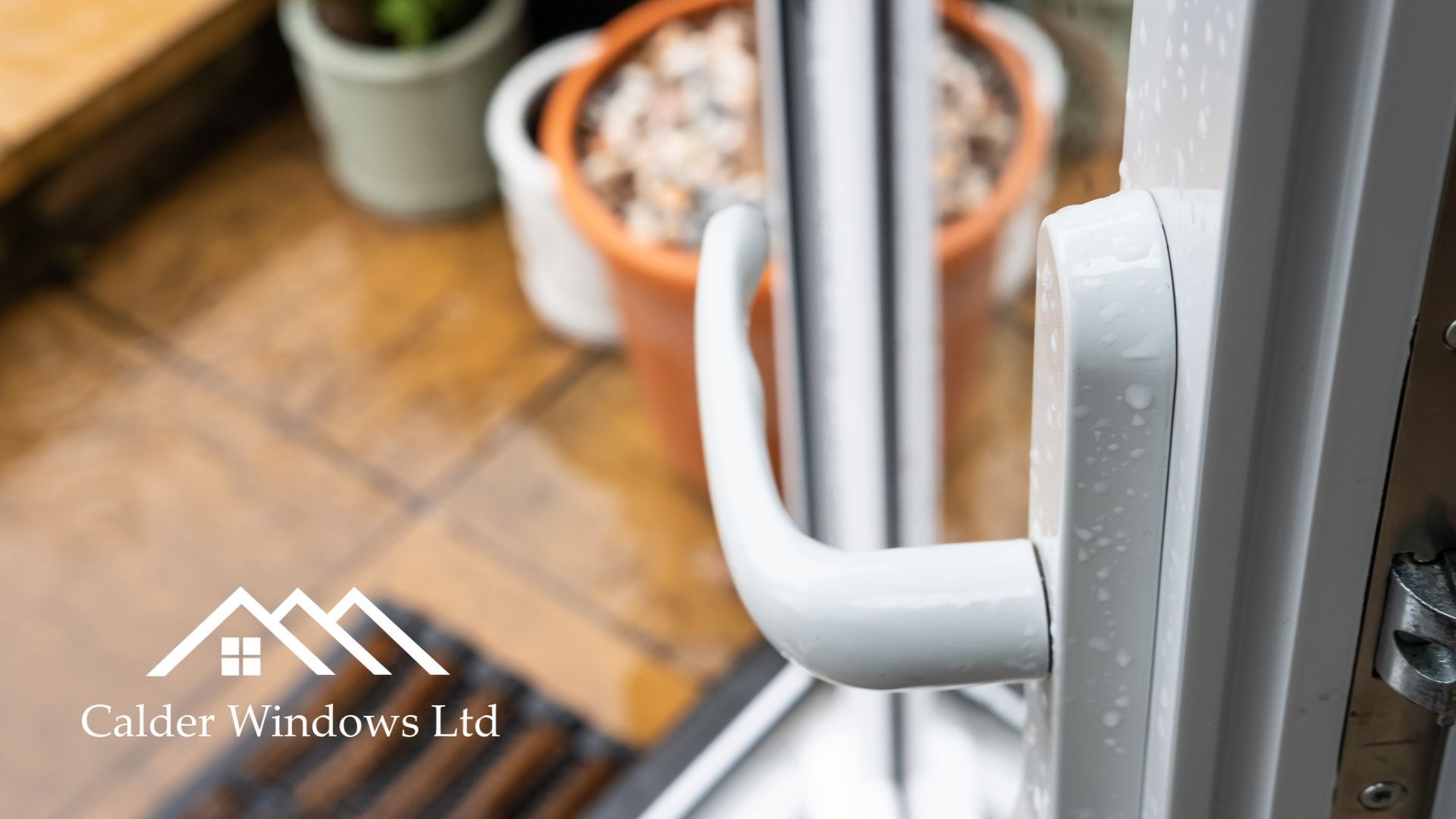 Close-up of a white door handle on a glass door, with potted plants blurred in the background.