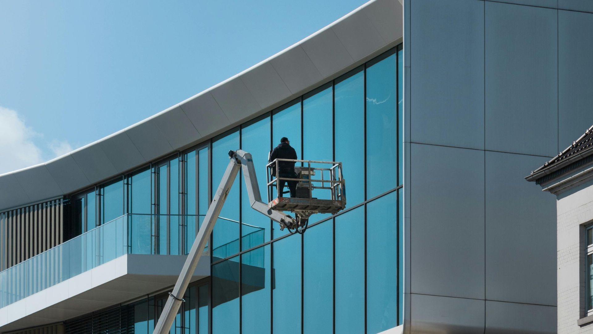 Worker in a lift painting a modern building’s blue glass and gray facade