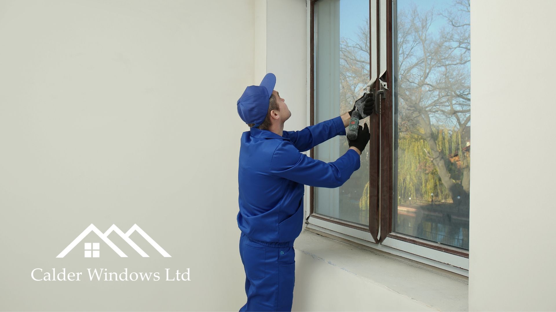 Worker in blue uniform cleaning a window with a squeegee indoors.