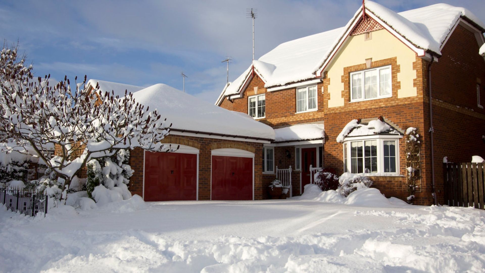 Snow-covered brick house with red garage doors and a white-trimmed entry under a bright winter sky.