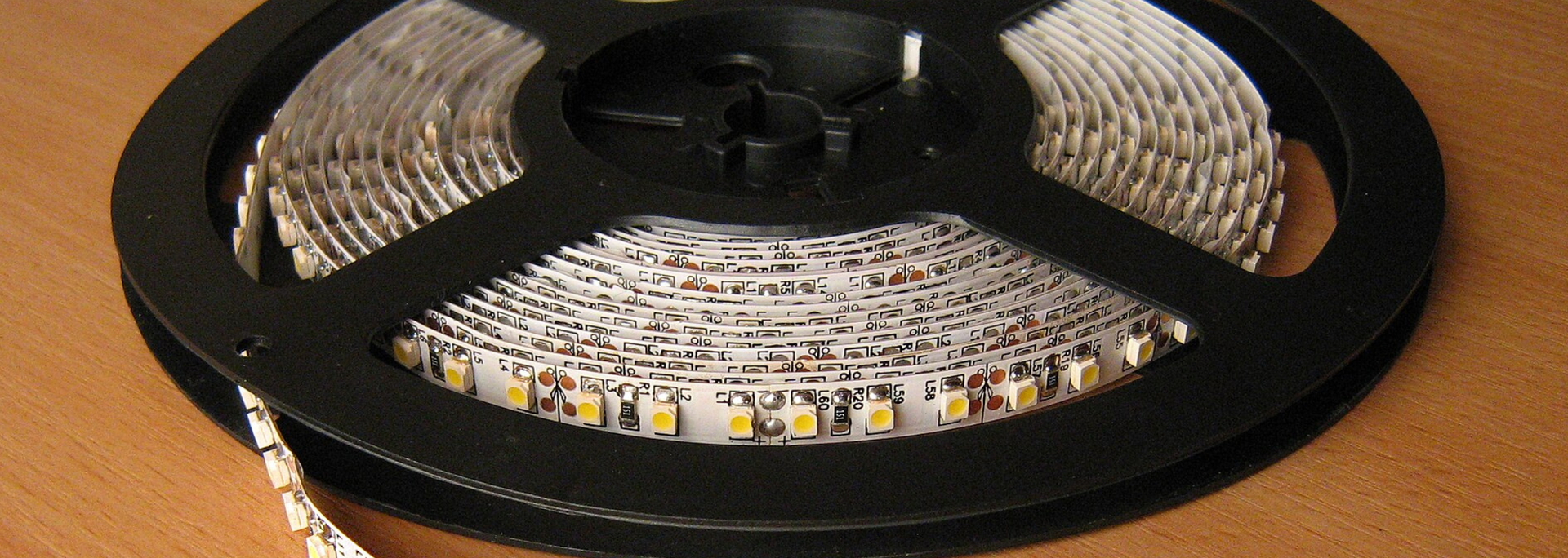 Spool of white LED strip lights on a black reel on a wooden surface