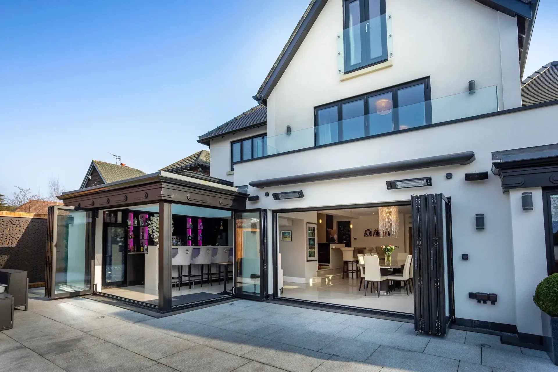 Modern white house exterior with open glass doors and a small patio area