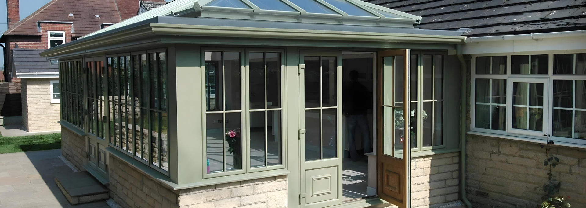 Glass conservatory attached to a brick house with a green roof and white-framed windows
