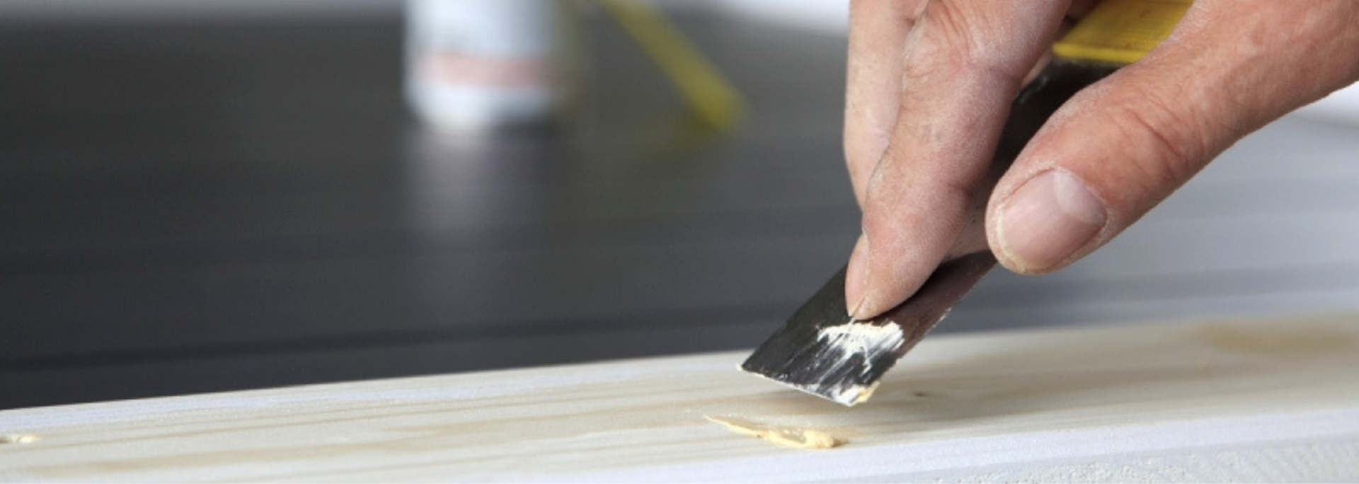 Hand sanding a white wooden surface with a small scraper or sandpaper block