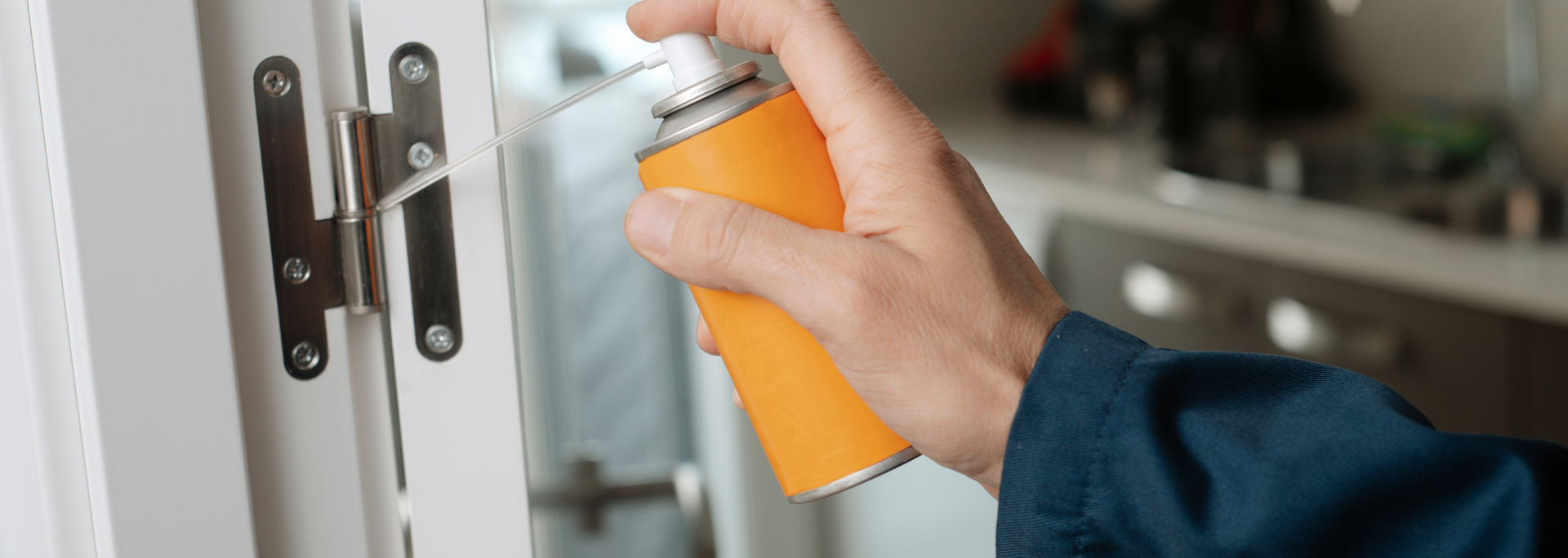 Hand holding an orange cleaning spray bottle beside a white door handle and lock