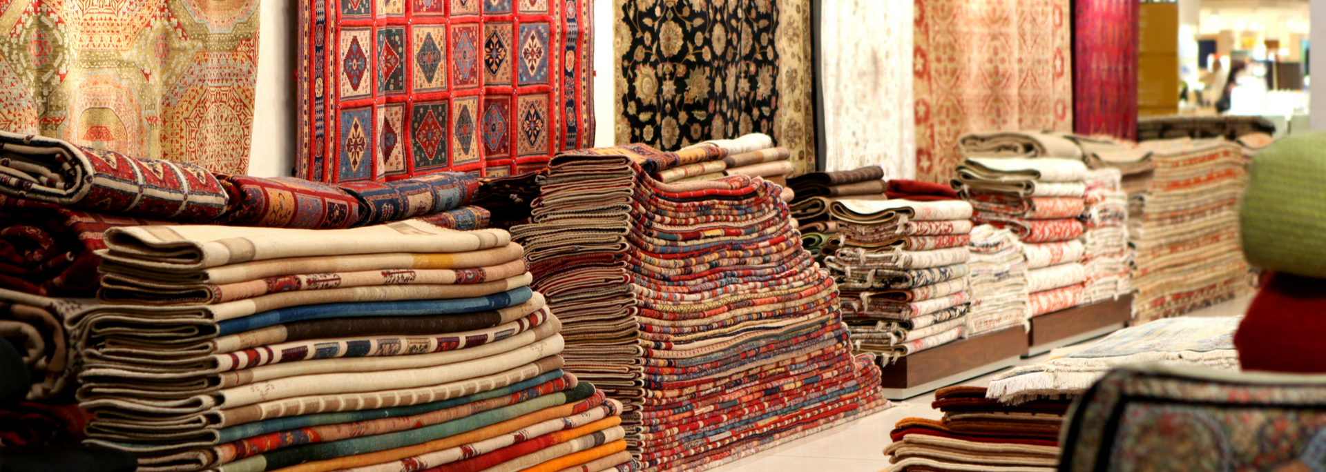 Stacks of colorful folded textiles displayed in a market stall with patterned rugs and fabrics in the background
