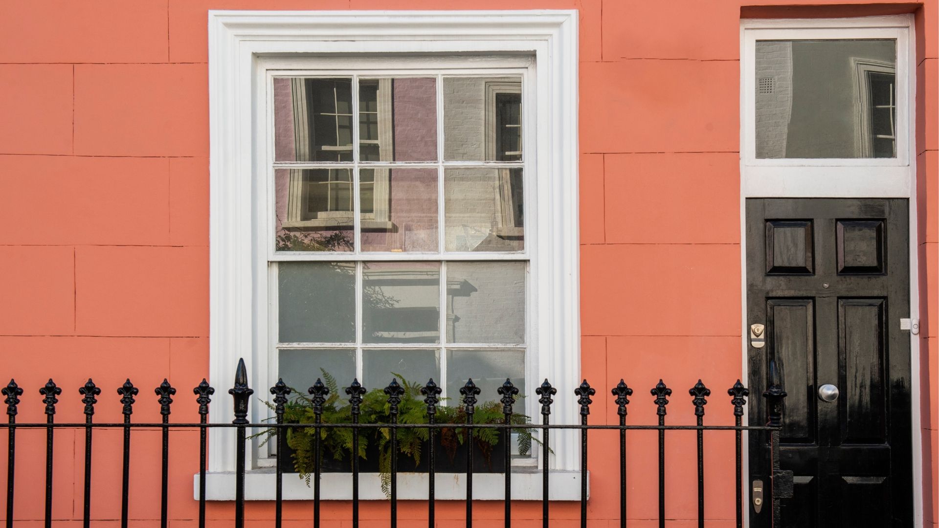 Coral townhouse facade with white-trimmed window, black door, and black wrought-iron fence