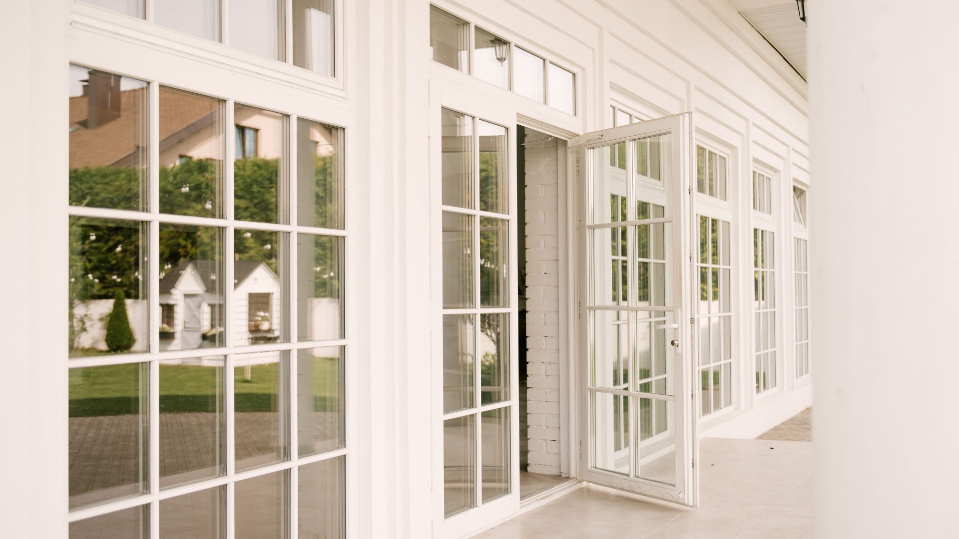 White-trimmed glass doors and windows opening onto a bright covered porch with a view of a green lawn.