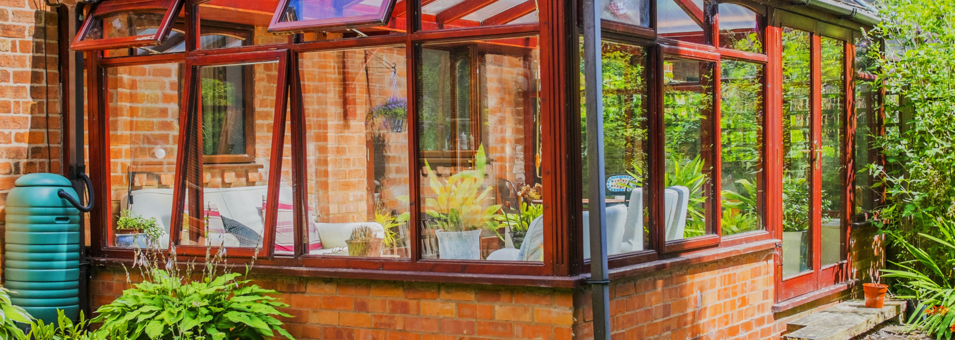 Brick-and-glass greenhouse with red metal frame, wooden trim, and green plants inside
