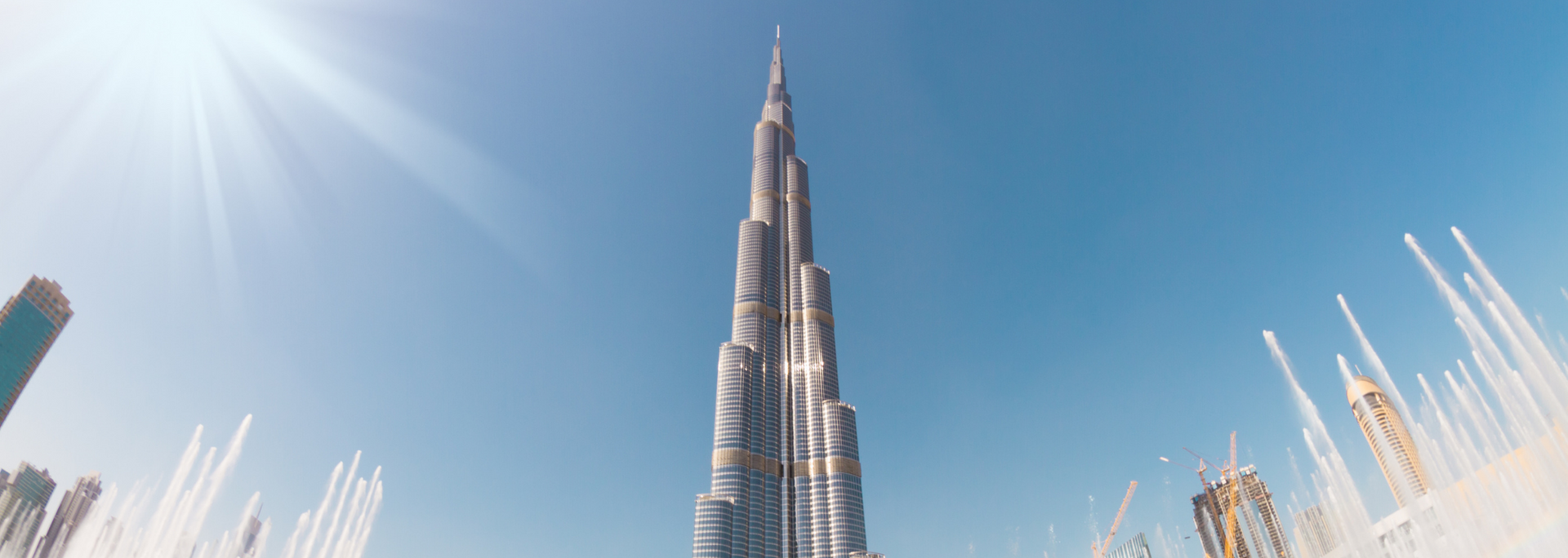 Burj Khalifa towering over Dubai skyline under a bright blue sky with sun flare
