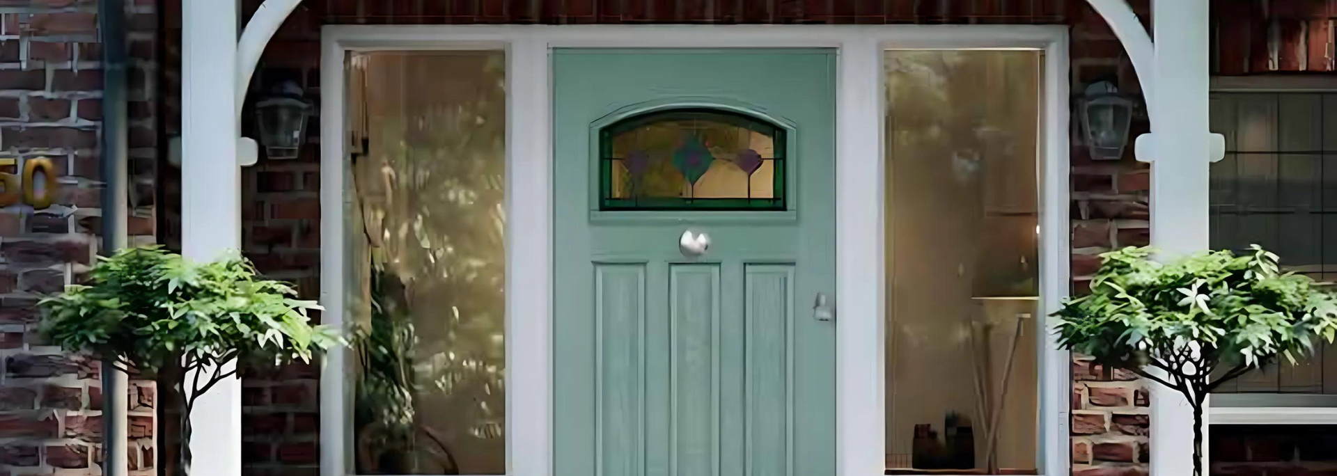 Mint-green front door with glass sidelights and potted plants beside a brick house entrance