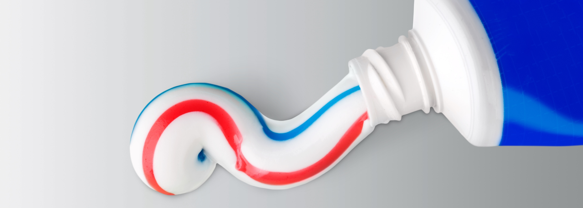 Red and blue toothpaste squeezed from a white tube onto a gray surface