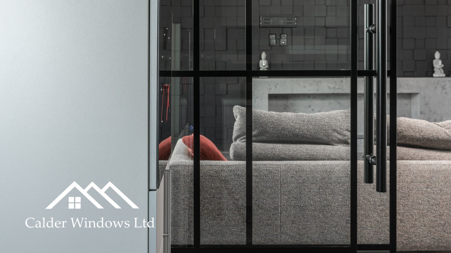 Modern bedroom with a gray bed behind black-framed glass doors and a white wall logo.