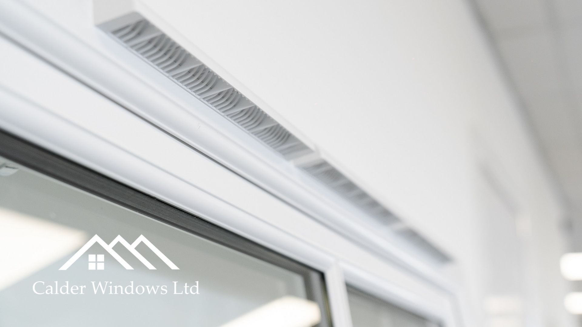 White wall-mounted air vent above a window in a bright interior room