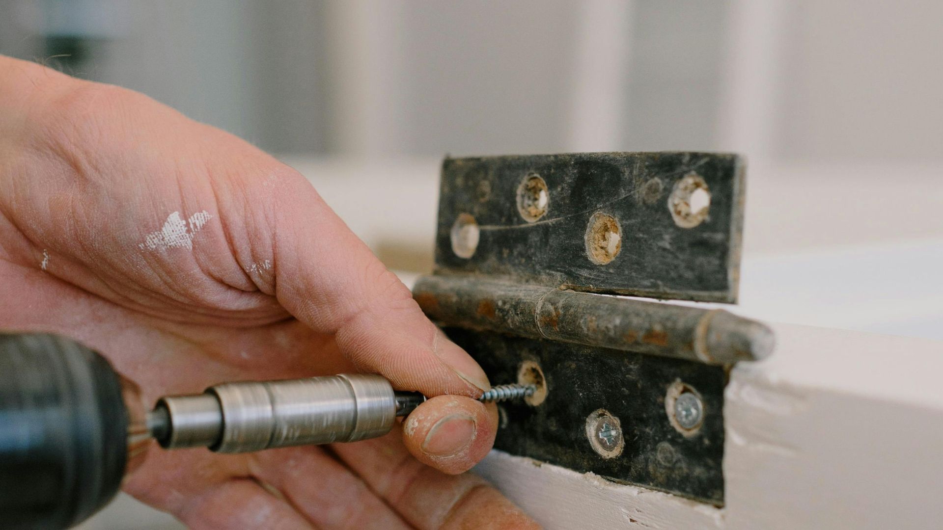 Hand using a tool to repair a black metal hinge with exposed screws