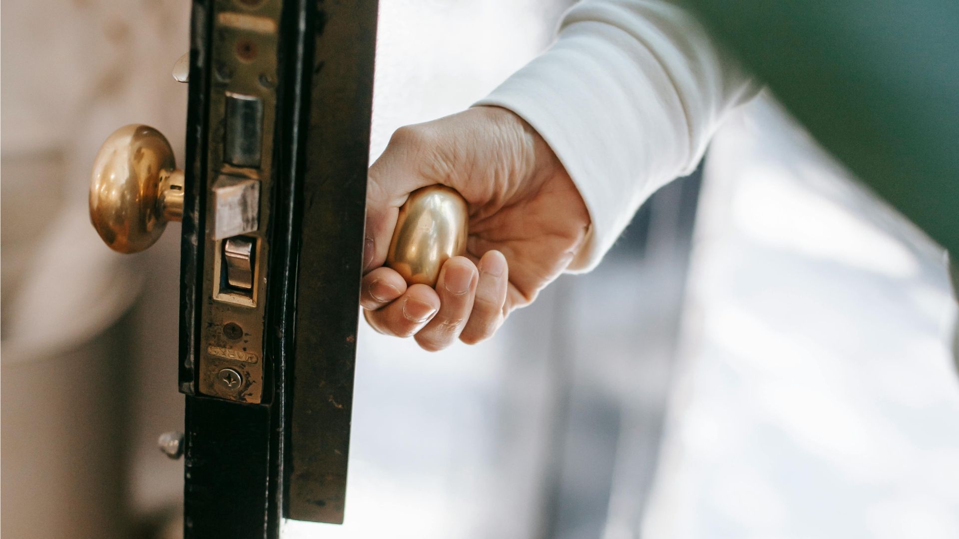 Hand turning a brass door knob to open a black-framed door