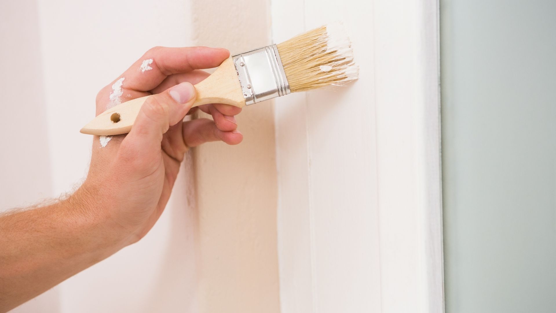 Hand painting a white wall with a brush, applying light paint near the edge
