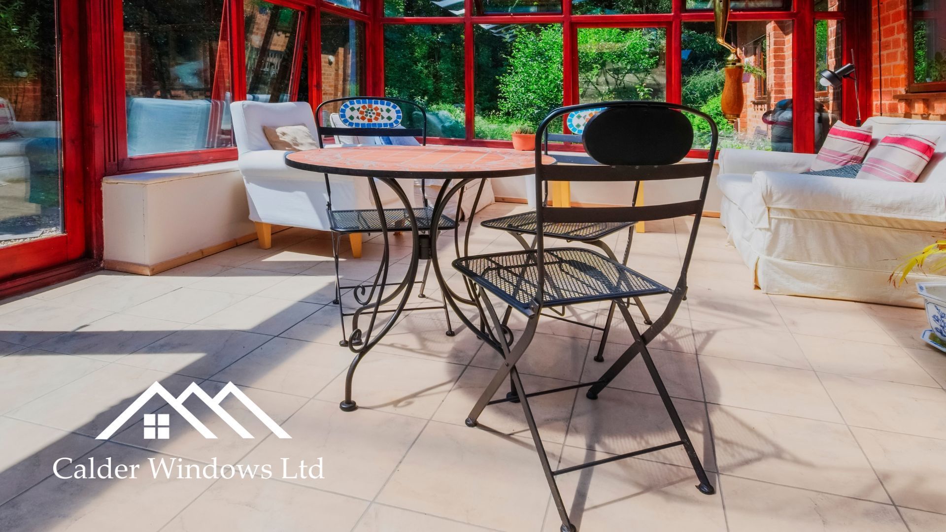 Patio with black metal bistro table and chairs on a tiled terrace with red-framed windows and white seating