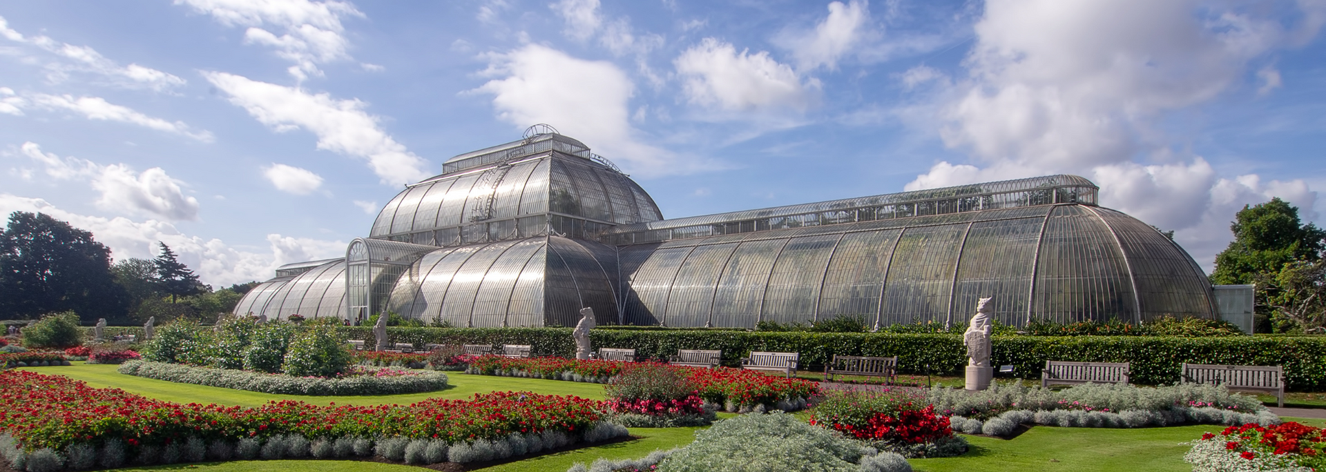 Glass greenhouse conservatory with arched roofs, set behind a colorful flower garden