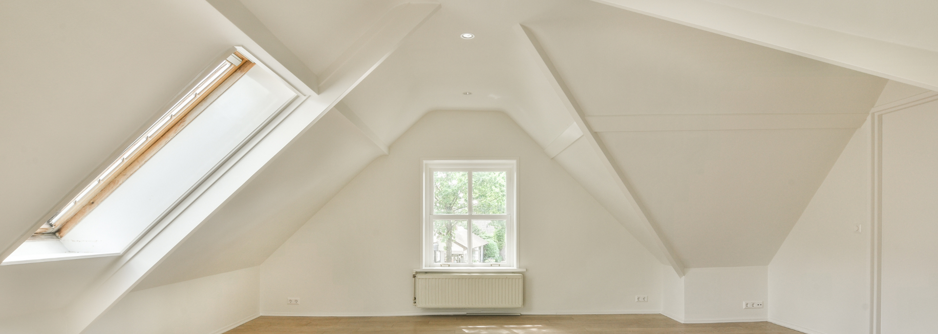 White attic room with slanted ceiling, skylight window, and a small central window above a radiator