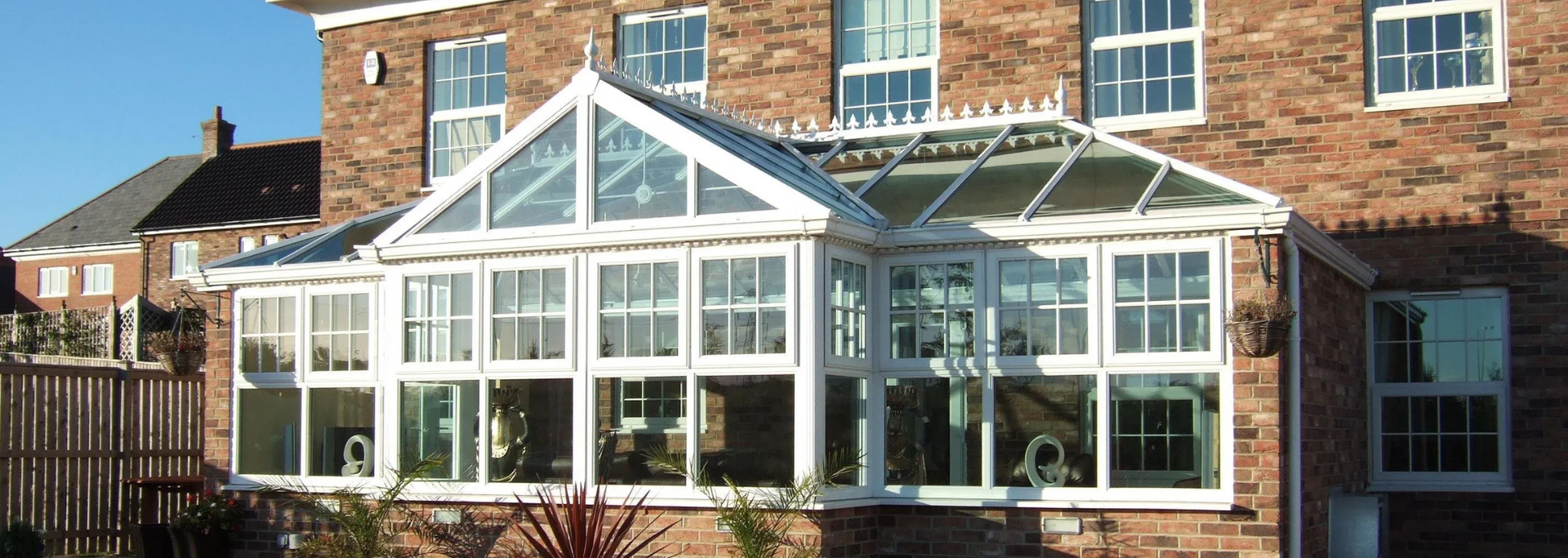 Glass conservatory attached to a brick house, with white framing and a sunny exterior.