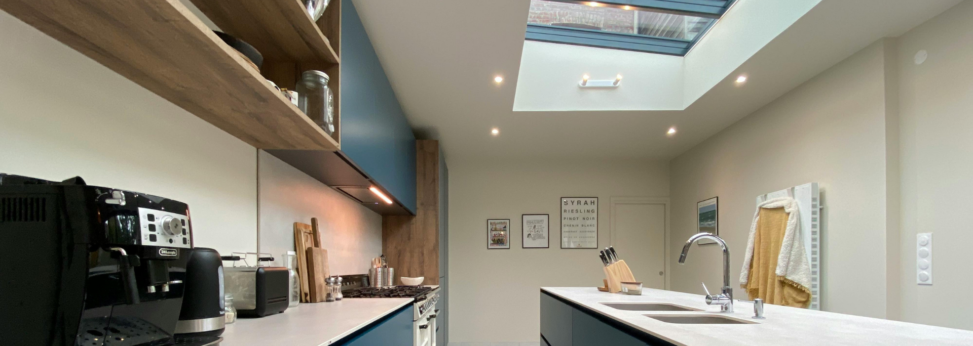 Modern office with a long wooden shelf, laptop, white desk, and skylight ceiling; a dog stands near the desk.