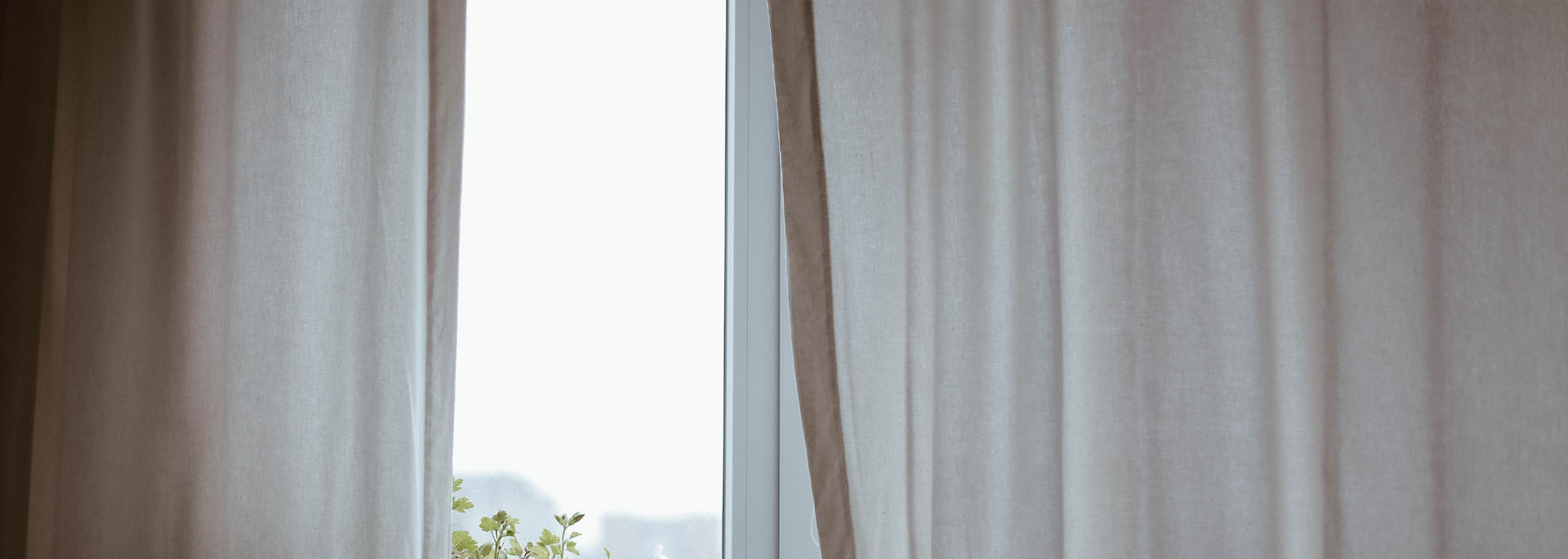White curtains framing a bright window with a small view of trees and sky outside