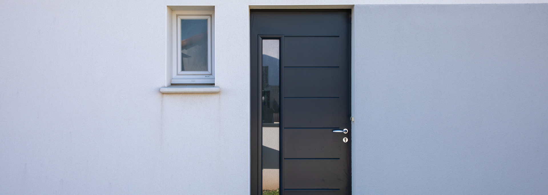 Minimalist white exterior wall with a small window and a dark gray front door