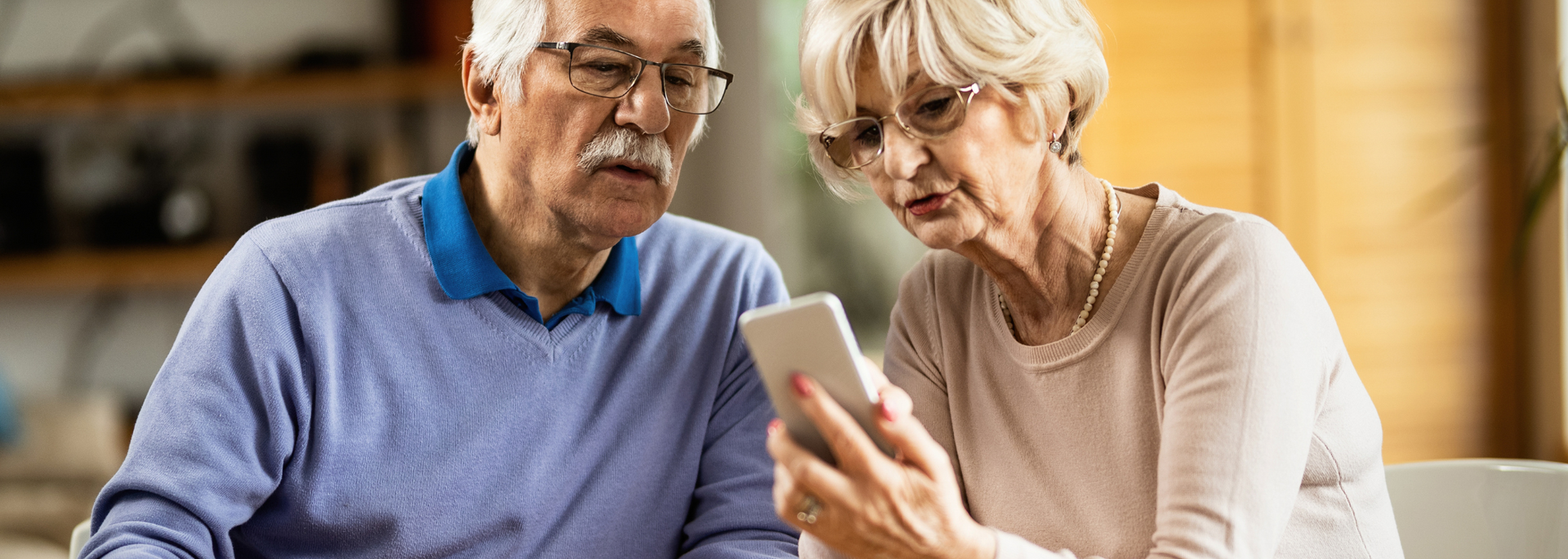 Two older adults reviewing a smartphone together in a bright living room