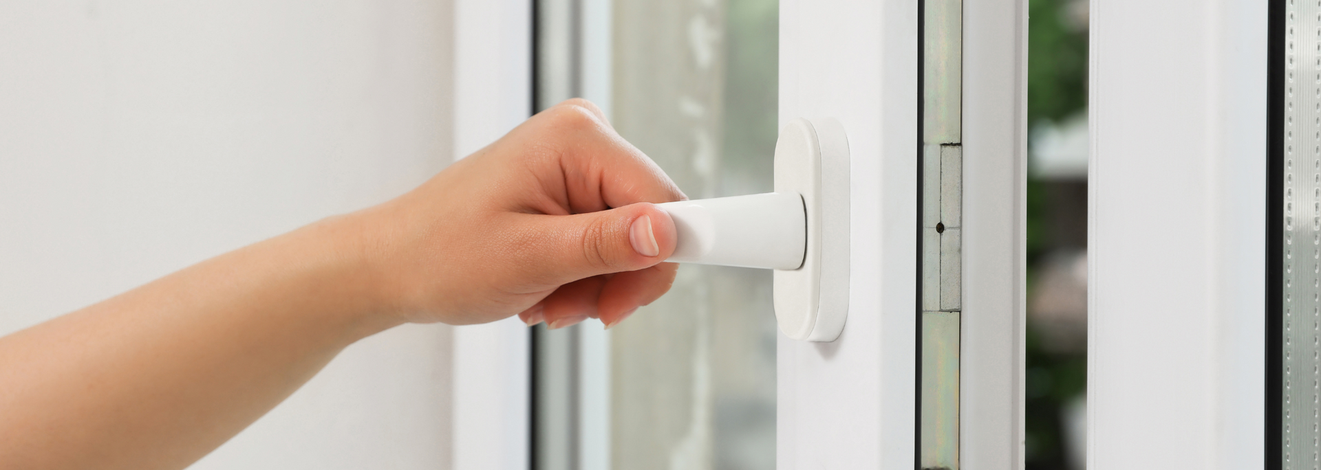 Hand turning a white window handle on a glass door frame
