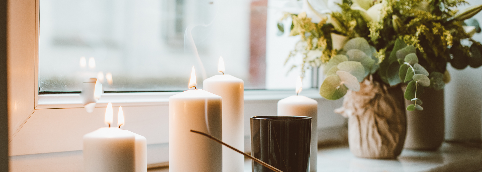 Lit candles and a flower vase on a windowsill in a softly lit room