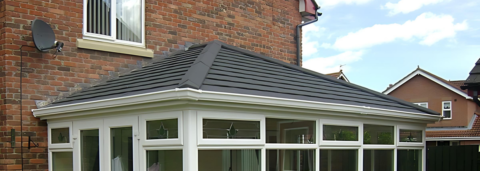 White conservatory attached to a brick house, with a dark gray tiled roof and large windows