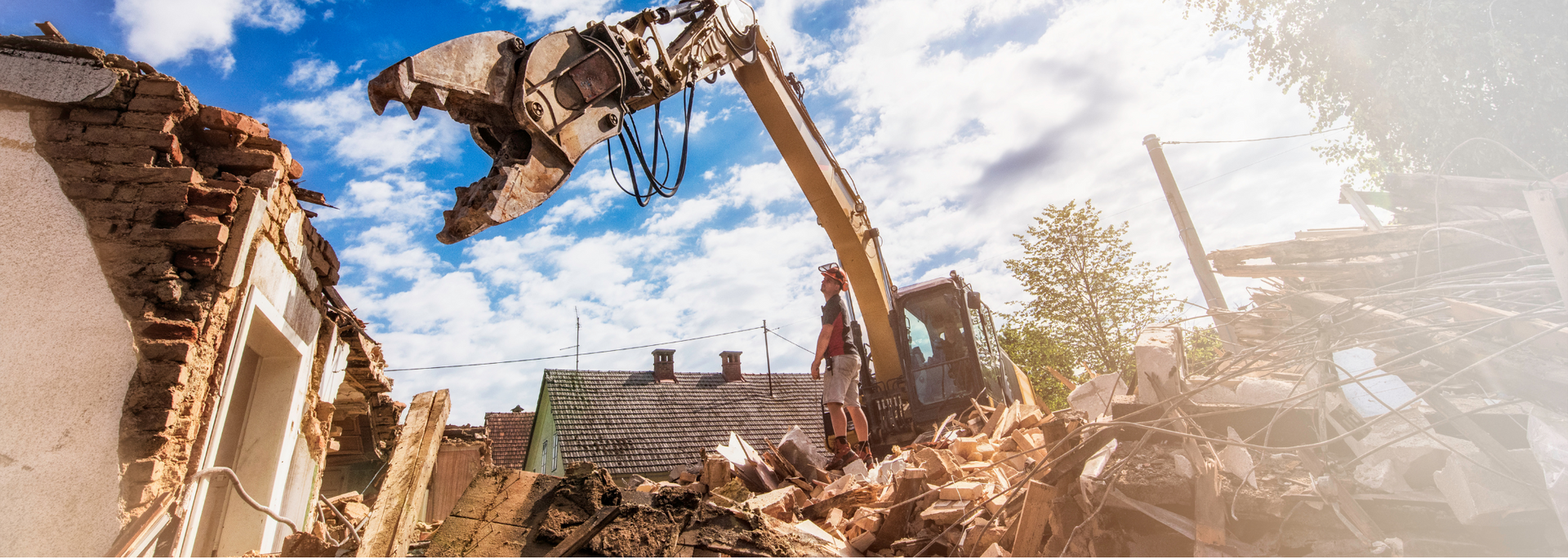 Excavator demolishing a partially collapsed building amid rubble and dust