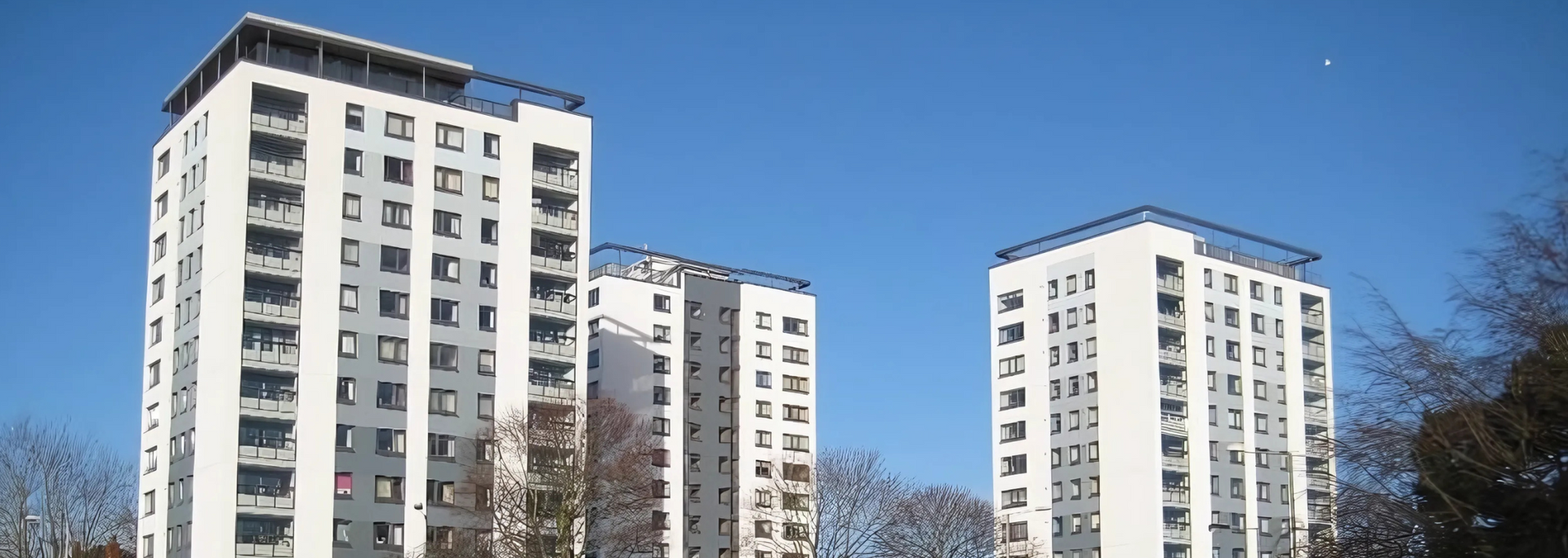 Three white apartment towers against a clear blue sky.