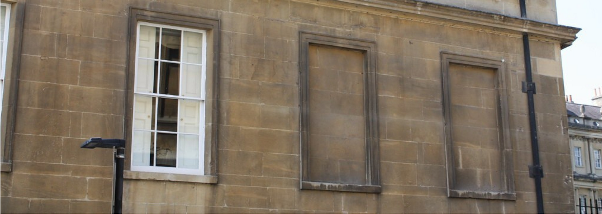Stone building facade with white-framed window and two boarded-up window openings