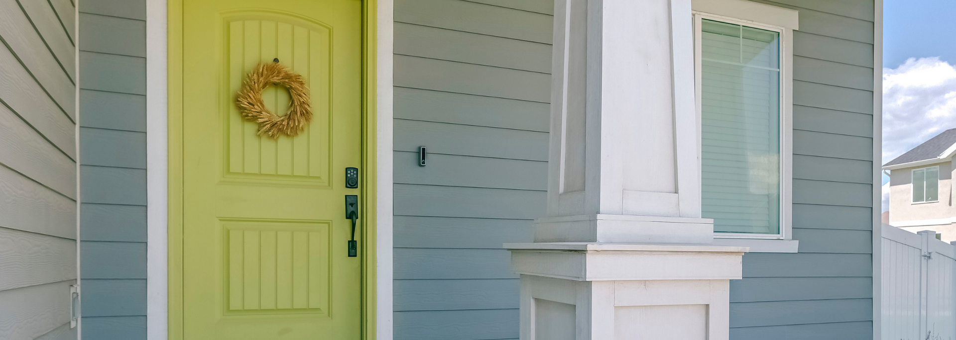 Lime green front door with wreath beside a white bay window on a light blue house exterior