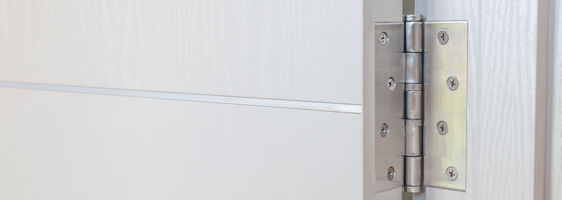 Close-up of a silver metal door hinge on a light-colored door frame