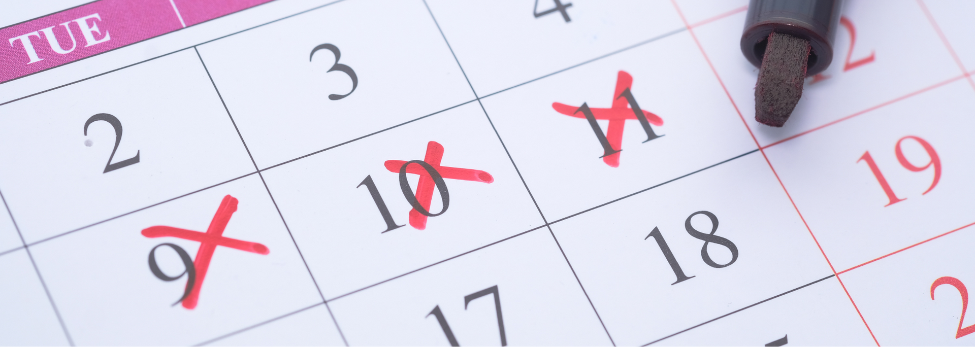 Close-up of a calendar with several dates crossed out in red and a pencil pointing at a day