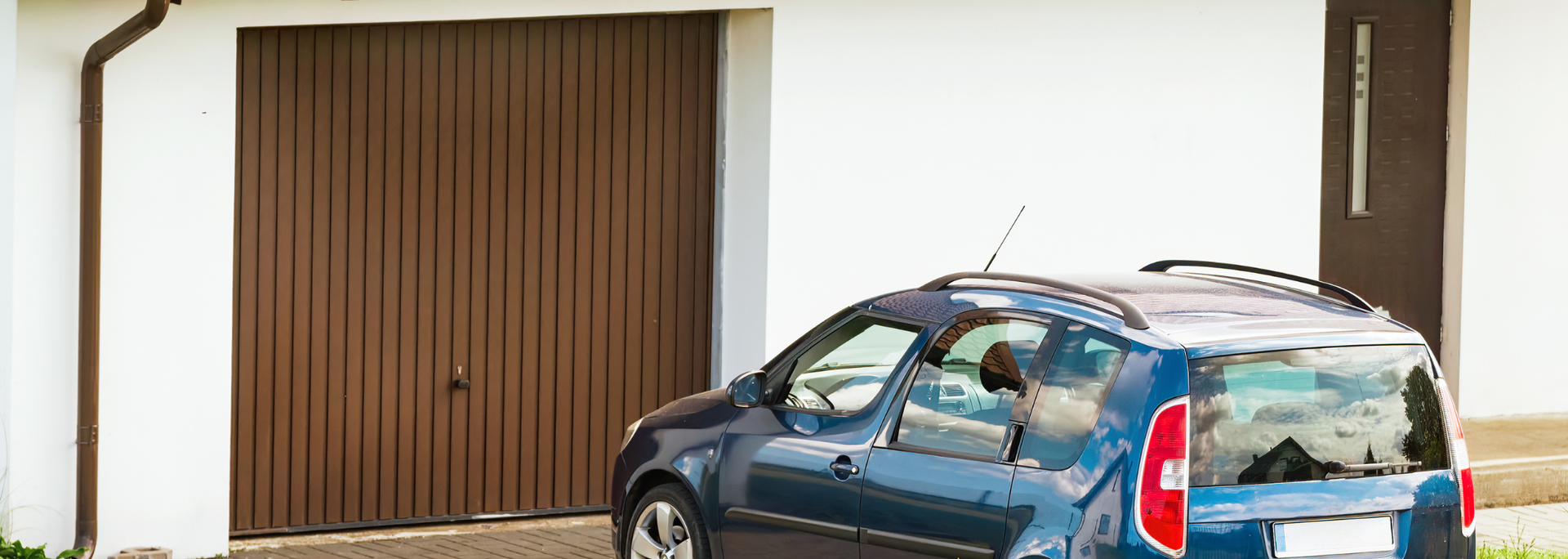 Blue car parked in front of a brown garage door in a white building