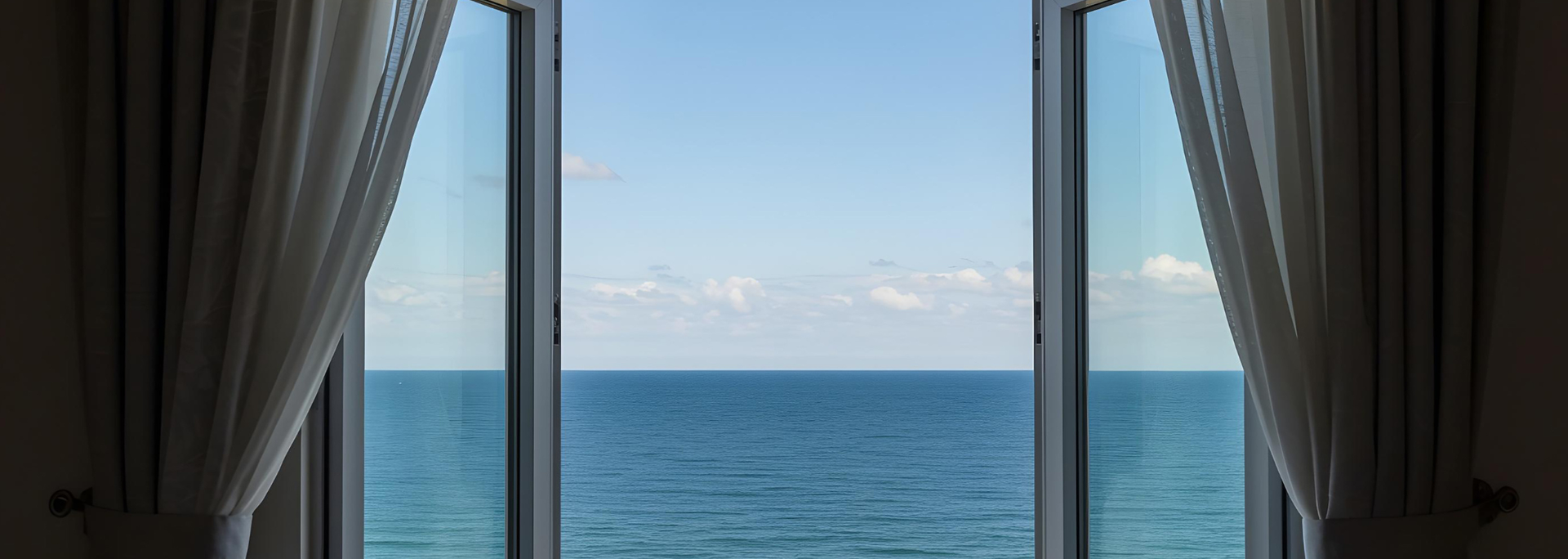 Curtains framing a window with blue ocean and sky beyond