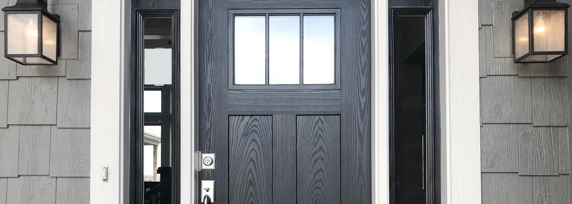 Front entry with dark double doors, sidelights, and wall lanterns on a gray stone exterior
